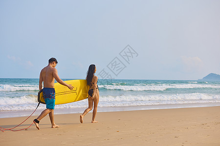 男女性感年轻男女拿着冲浪板海边行走背影背景