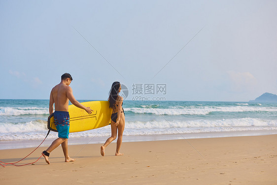 年轻男女拿着冲浪板海边行走背影图片