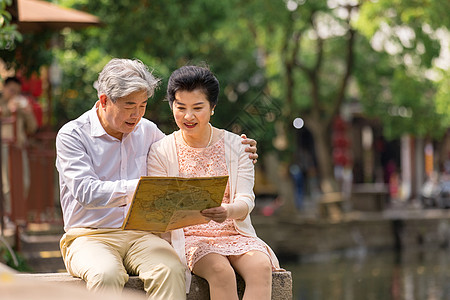 老年夫妻坐在河畔看地图高清图片