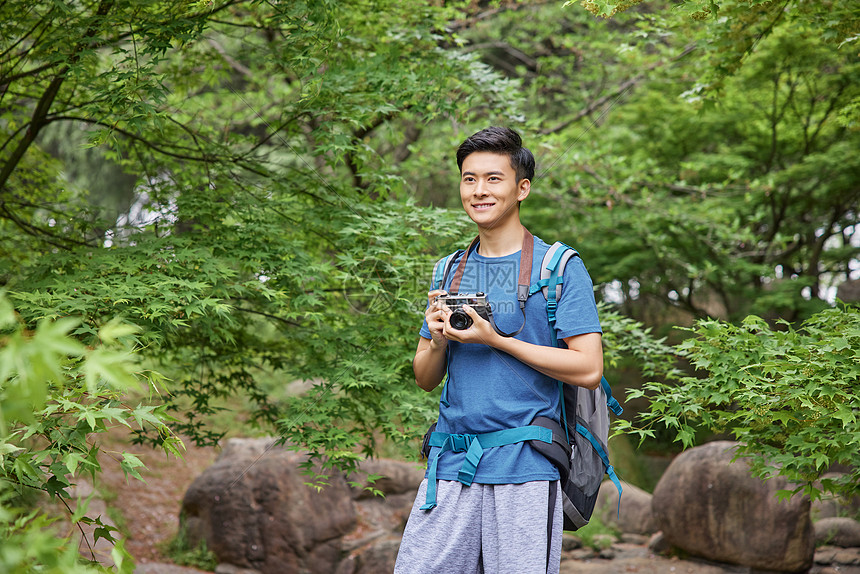 青年男性户外徒步拿相机拍照图片