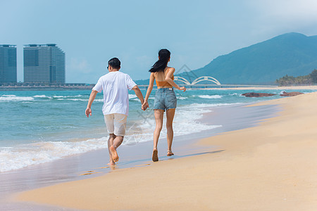 三亚水上旅游夏日情侣海边沙滩牵手散步背景