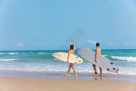 美女海边行走情侣拿着冲浪板海边沙滩上行走背景