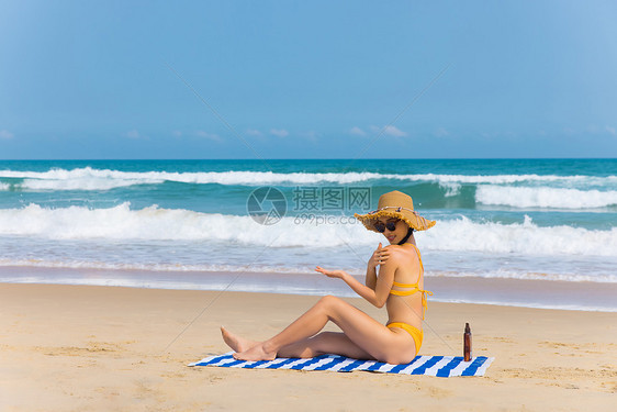 戴草帽比基尼美女沙滩上涂抹防晒图片