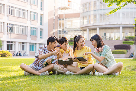 年轻大学生坐在草坪上嬉笑讨论高清图片