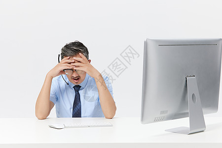 在电脑上前工作的中年男客服表情苦恼图片