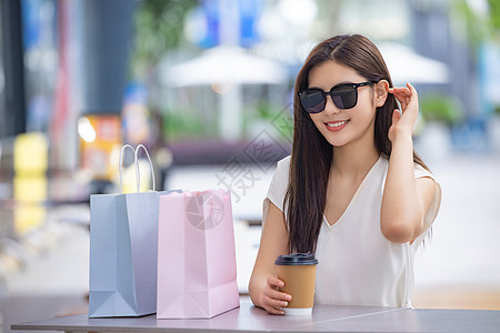 戴墨镜的美女购物消费坐在室外咖啡厅图片