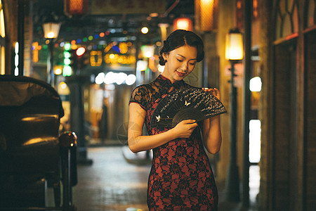 城市夜晚霓虹灯下手拿扇子的旗袍美女背景