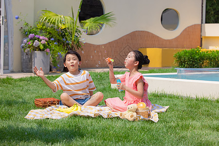 小男孩与小女孩草坪上野餐吹泡泡图片