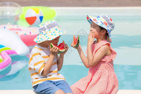 小男孩和小女孩面对面坐在泳池旁开心吃西瓜背景图片