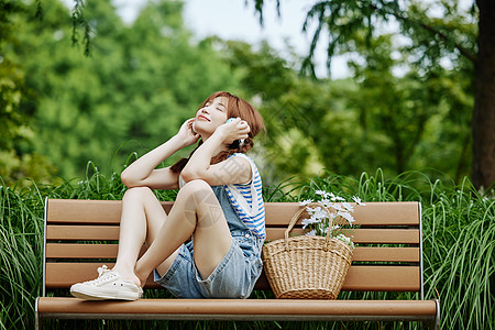 听音乐女孩坐在长椅上听音乐的夏日美女背景