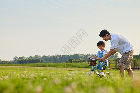 爸爸和孩子骑车年轻爸爸陪伴小男孩学骑自行车背景