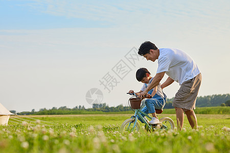 爸爸和孩子骑车年轻爸爸陪伴小男孩学骑自行车背景