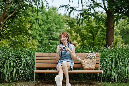 手拿相机坐在长椅上的夏日美女图片