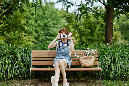 手拿相机坐在长椅上的夏日美女图片