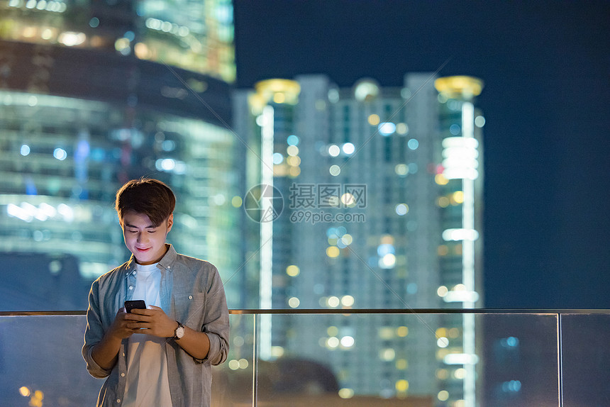 夜晚城市里看手机的男青年图片