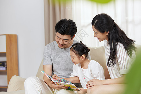 室内幸福的一家人一家三口在沙发上看故事书背景