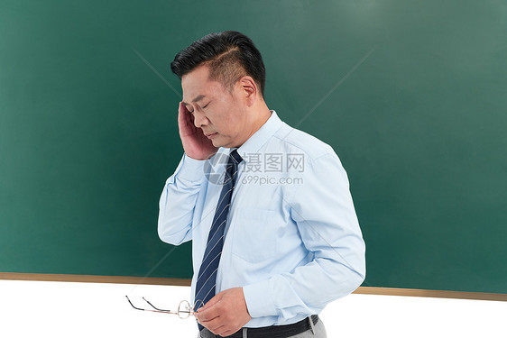 中年教授在黑板前摘下眼镜按摩太阳穴图片