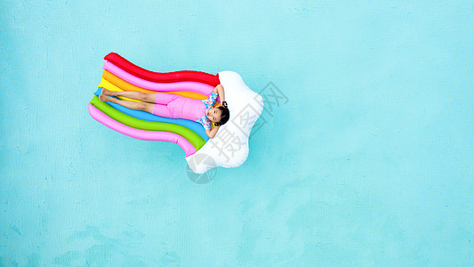 儿童小女孩躺在泳池彩虹气垫床上俯拍图片