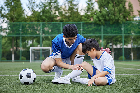 足球运动员踢球父亲给男孩检查受伤的膝盖背景