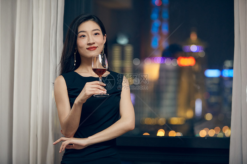 气质美女夜晚端着红酒杯站在窗前图片