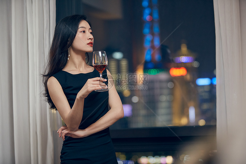 气质美女夜晚端着红酒杯站在窗前图片