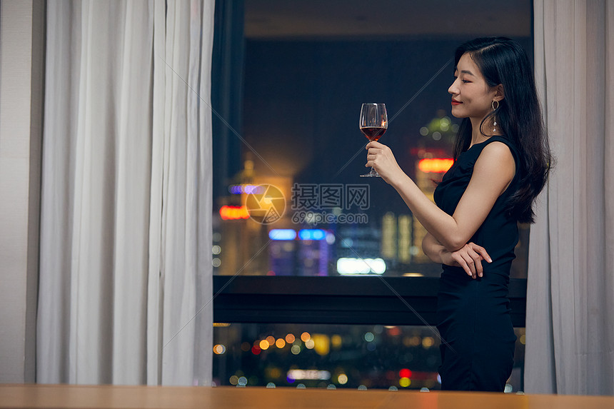 气质美女夜晚端着红酒杯站在窗前图片