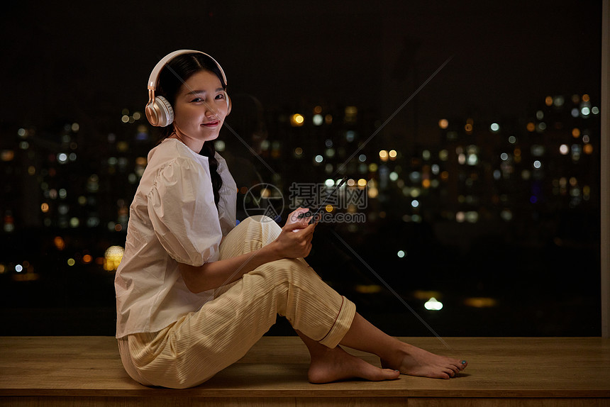 独居女性夜晚在窗边听歌