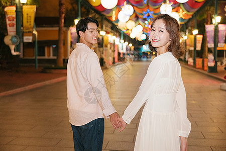 年轻情侣牵手走在商店街道上图片