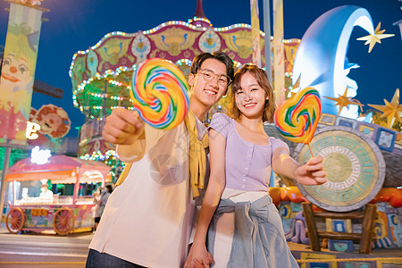 游乐场夜景拿着棒棒糖的年轻情侣在游乐园玩耍背景