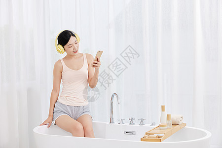 年轻女性坐在浴缸前玩手机听音乐图片