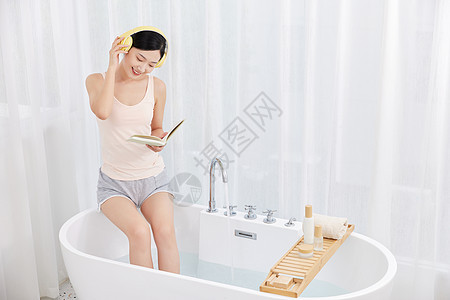 年轻女性坐在浴缸前看书听音乐图片