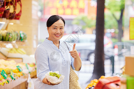 中年女性水果店内手拿葡萄点赞高清图片