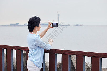 老年夫妻奶奶拿着手机对海边拍风景背景