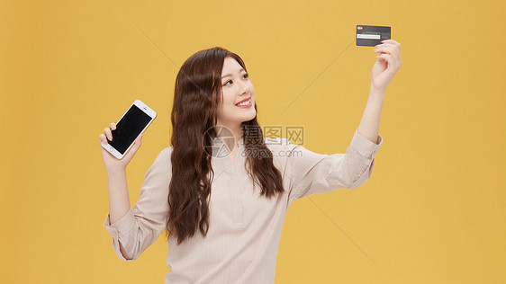 青年女性手拿信用卡和手机购物图片