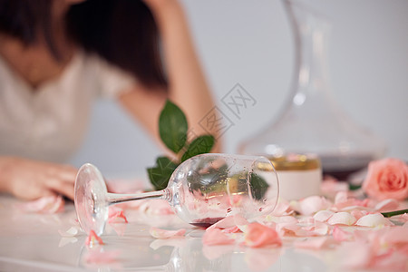 不舒服的美女桌子上散落的玫瑰花和酒杯特写背景
