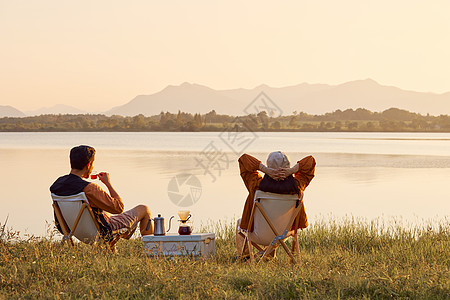 人群背影年轻情侣坐在湖边享受大自然背景