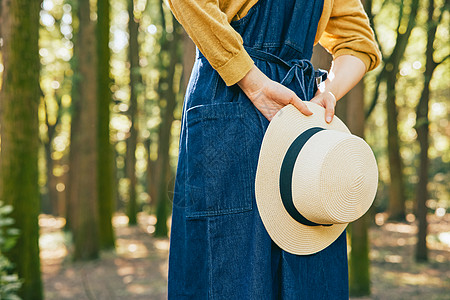 女性手拿草帽在森林里背影特写图片
