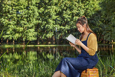 美女大学生公园湖边看书阅读背景