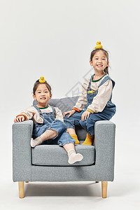 双胞胎小女孩坐沙发上玩小鸭子玩具图片