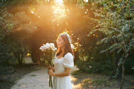 花裙子夕阳下拿着花的少女在微笑背景