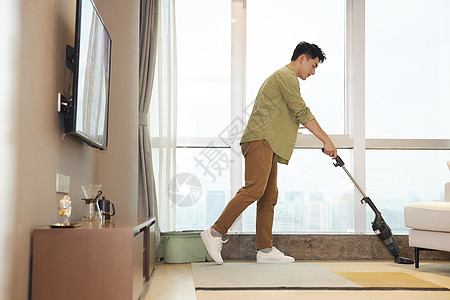 年轻男性居家使用吸尘器清洁地毯背景图片