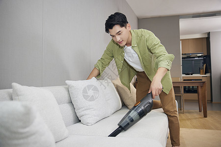 男青年使用吸尘器清洁沙发背景图片