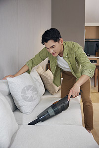 男青年使用吸尘器清洁沙发图片