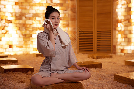 韩式汗蒸在桑拿房用毛巾擦汗的青年女性背景