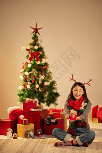 美女圣诞节手拿礼物坐在圣诞树和礼物前图片