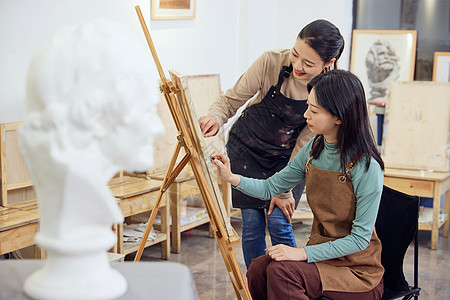 两个女人雕塑画室里老师指导学生画画背景