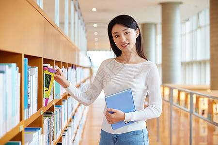 女学生手抱书籍女学生在图书馆书架前挑选书籍背景