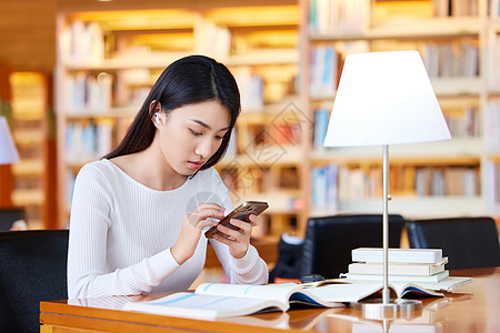 手机阅读女学生图书馆学习使用手机查资料背景