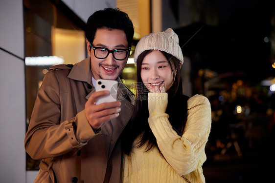 夜晚冬季情侣约会逛街看手机图片