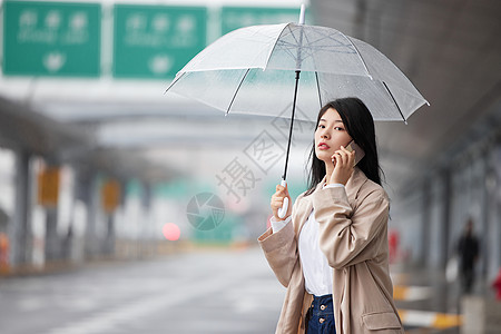 商务行李箱在机场外撑伞等车的女性背景